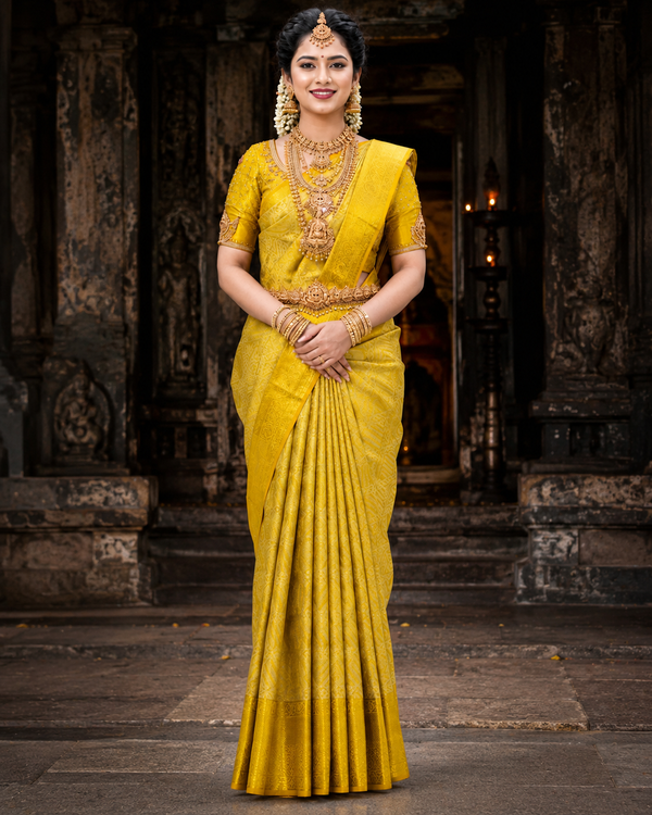 Woman in a yellow saree with traditional jewelry standing in front of an ancient temple.