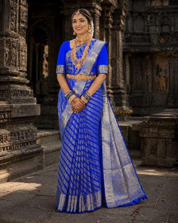 Woman in a blue saree with gold accents standing in front of an ancient architectural structure.