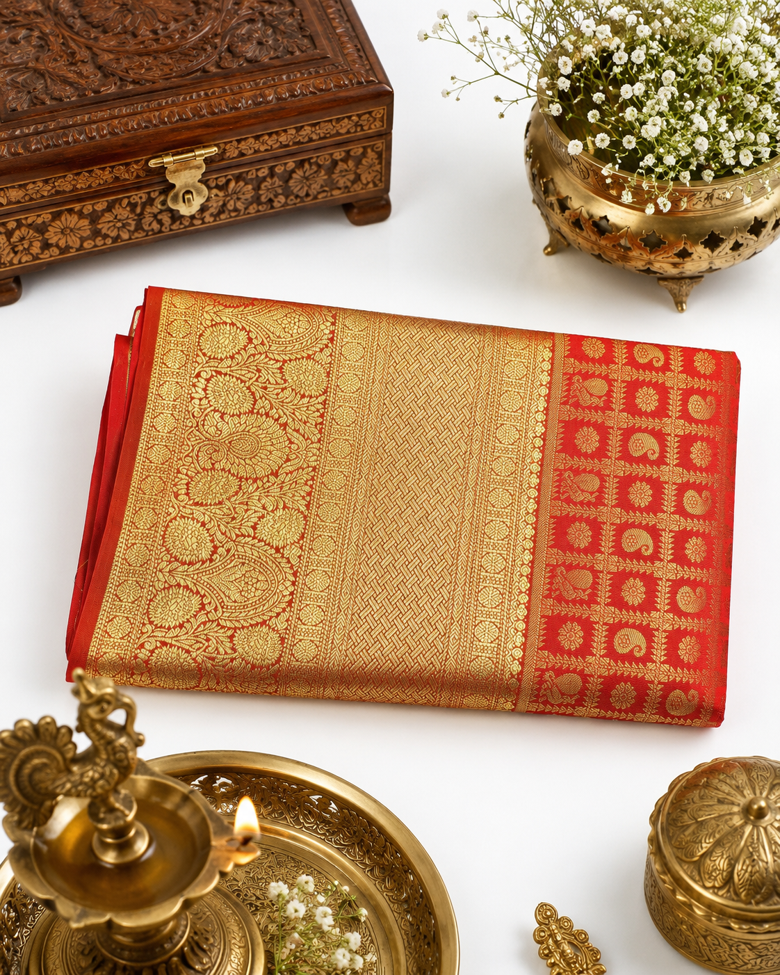 Decorative red and gold saree with ornate wooden box and brass items on a white background