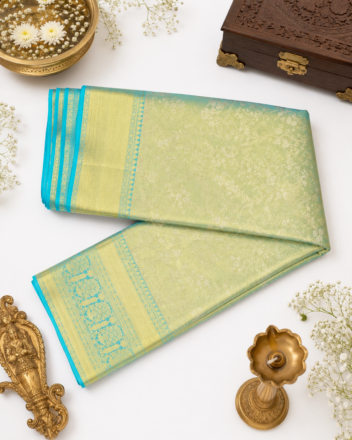 Green saree with blue border on a white background with decorative items.